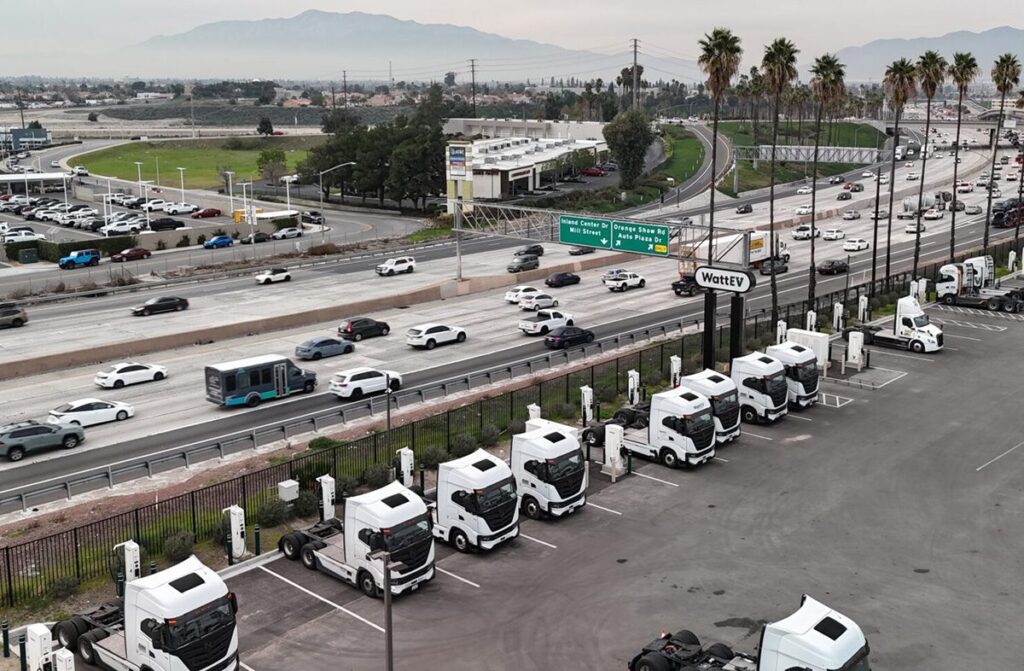 Parking lot of electric semi cabs charging at ports. The parking lot sits next to a southern California freeway.
